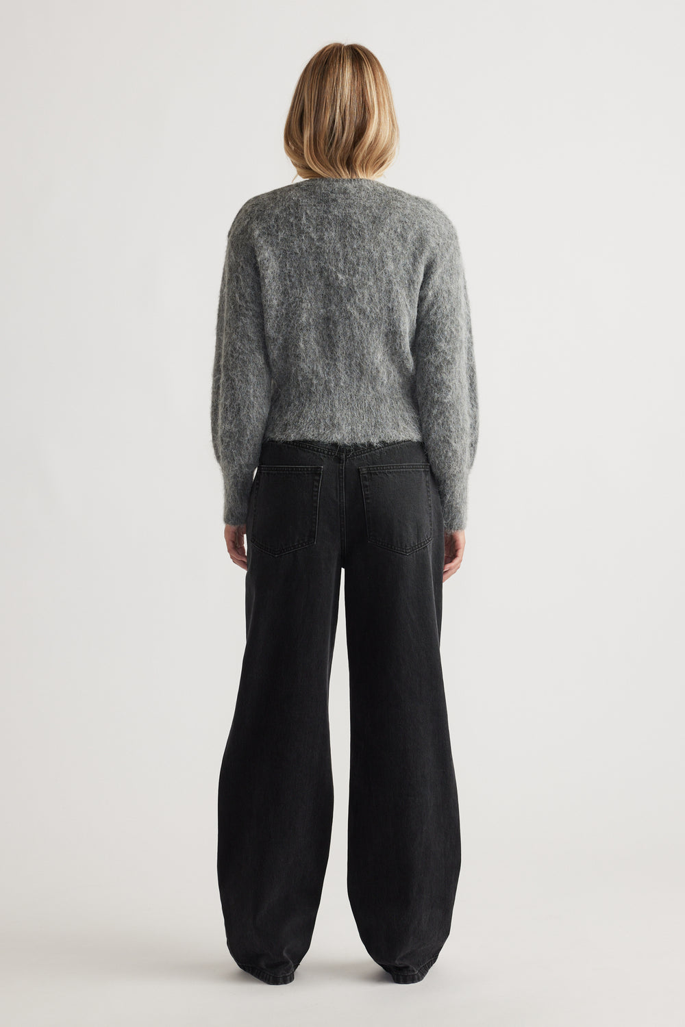 Woman seen from behind wearing a soft grey knit cardigan paired with relaxed black wide-leg denim jeans