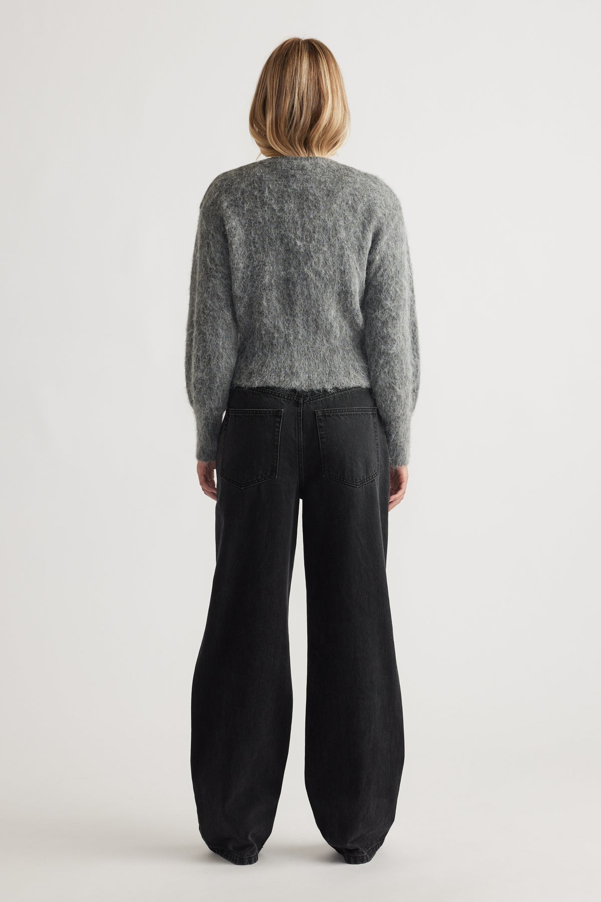 Woman seen from behind wearing a soft grey knit cardigan paired with relaxed black wide-leg denim jeans