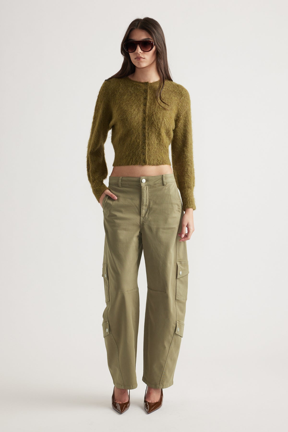 Woman wearing olive green barrel cargo pants with pockets, paired with a fuzzy cropped cardigan and sunglasses
