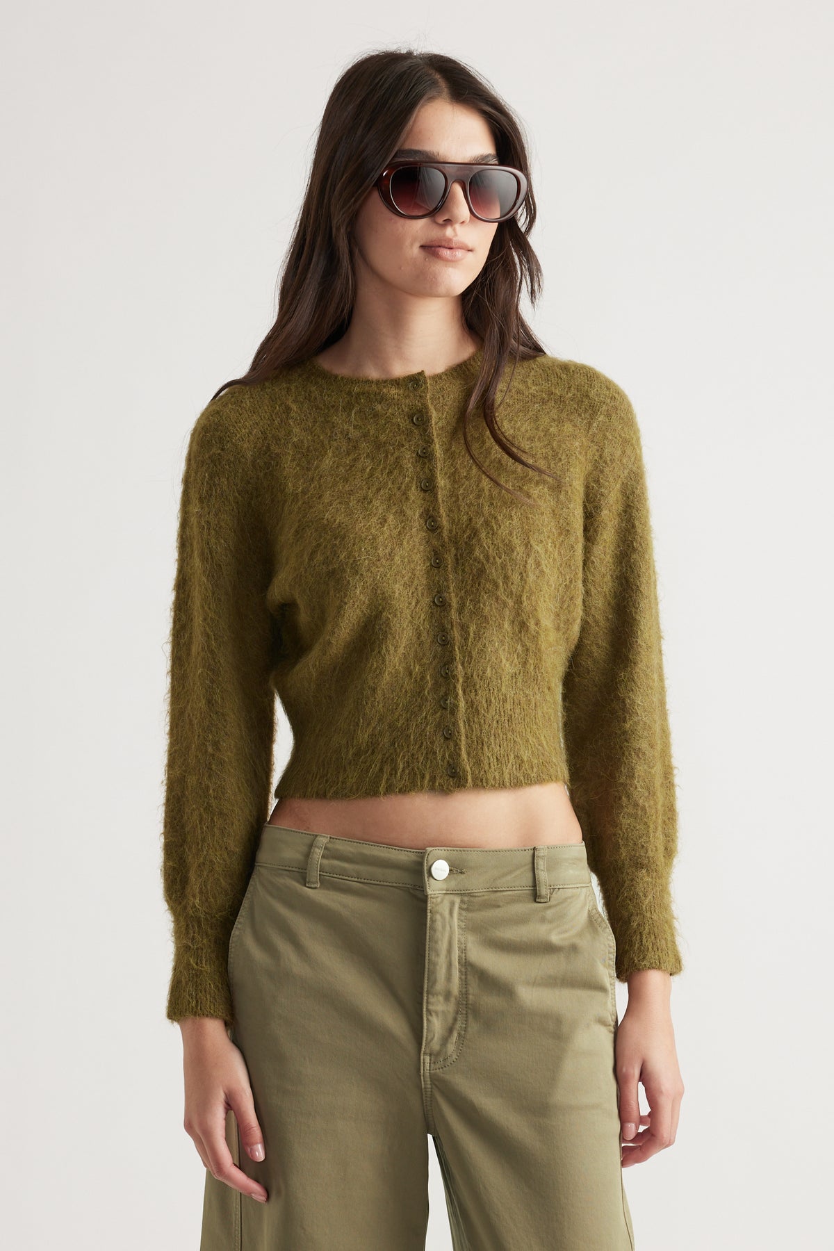 Woman wearing a textured olive green button-up cardigan with long sleeves and relaxed fit high-waisted pants