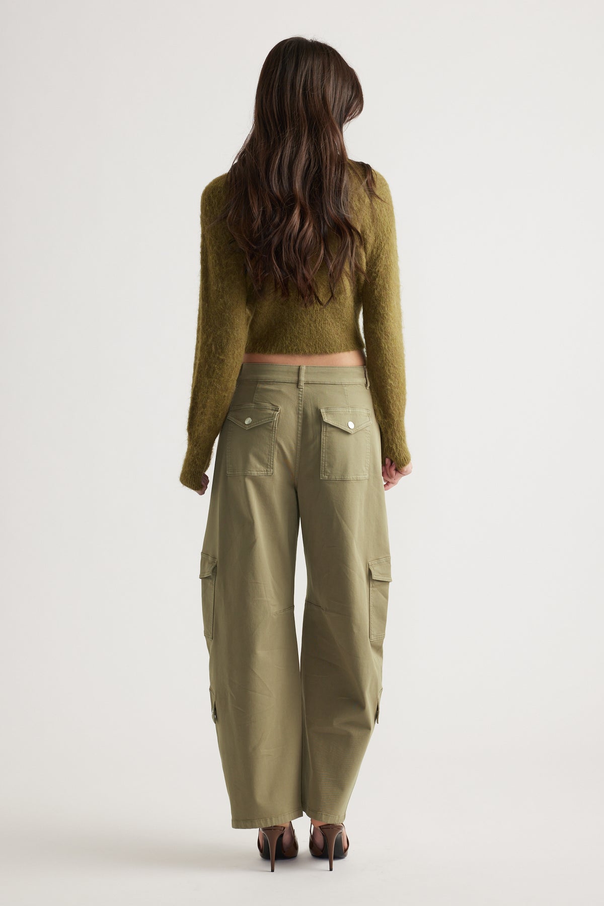 Woman wearing olive green cargo pants with flap pockets and a cropped fuzzy olive sweater, standing facing away