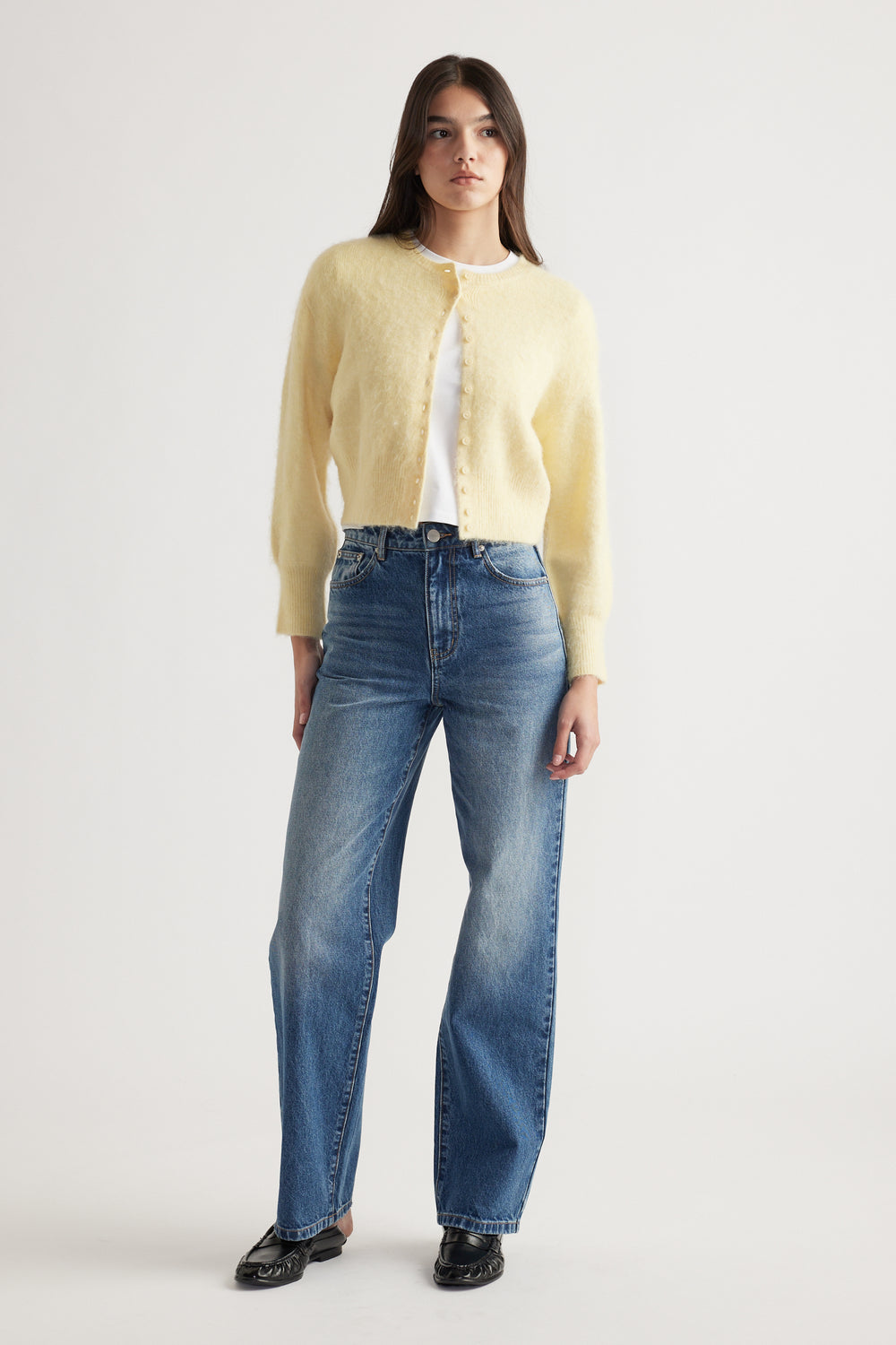 Woman wearing a soft lemon button-up cardigan paired with classic high-waisted blue denim jeans and black loafers