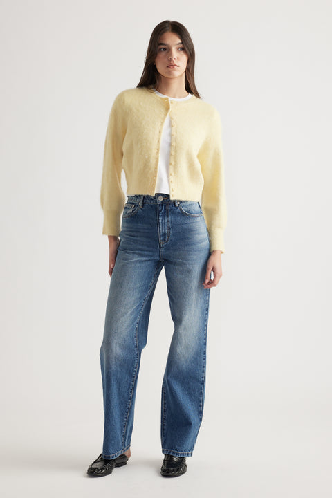 Woman wearing a soft lemon button-up cardigan paired with classic high-waisted blue denim jeans and black loafers