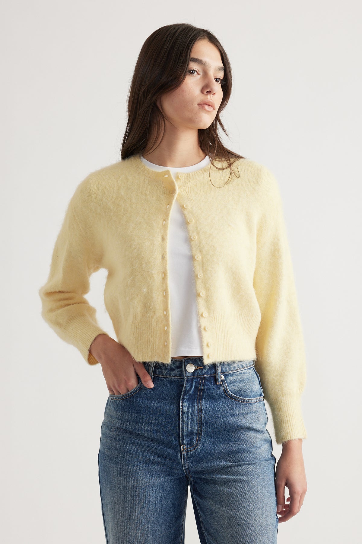 Woman wearing a soft yellow button-up cardigan over a white top paired with classic blue high-rise jeans