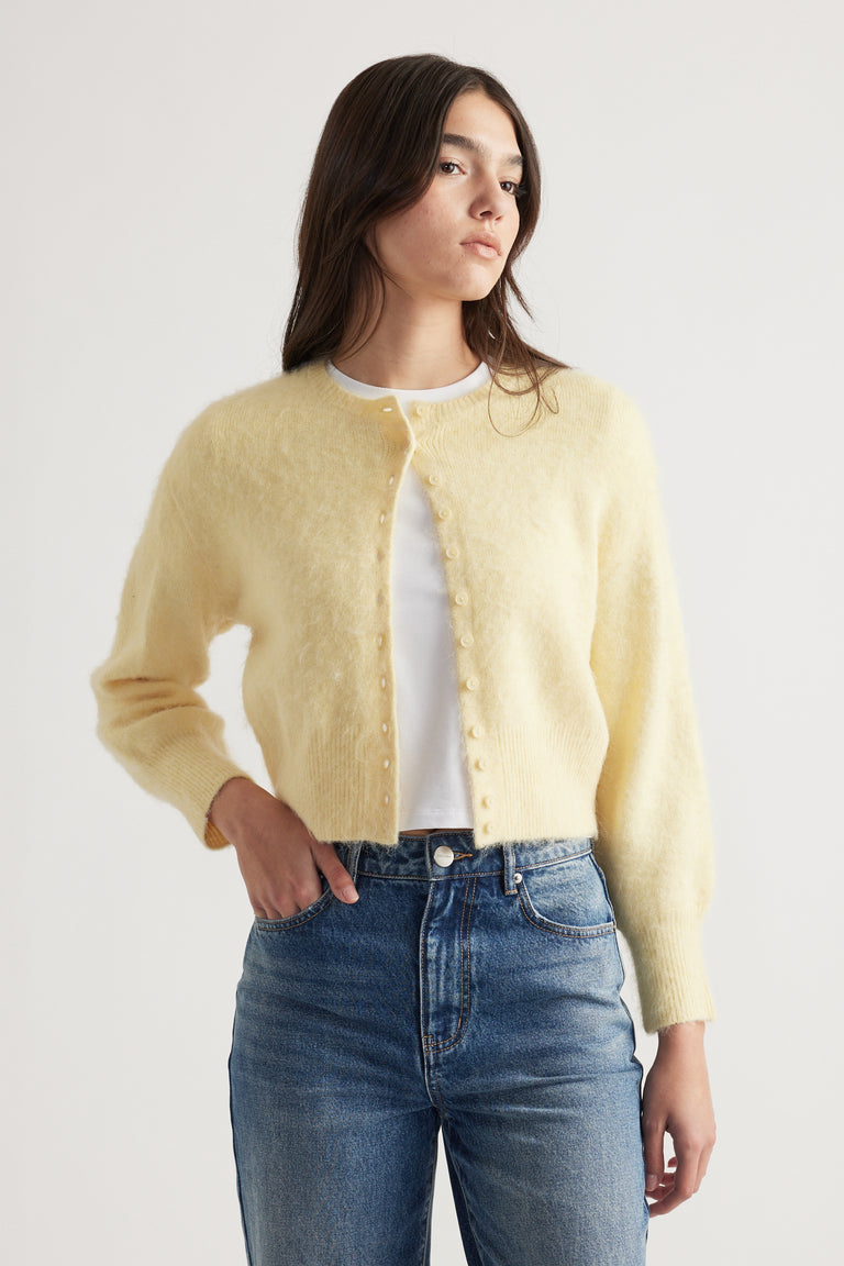 Woman wearing a soft yellow button-up cardigan over a white top paired with classic blue high-rise jeans