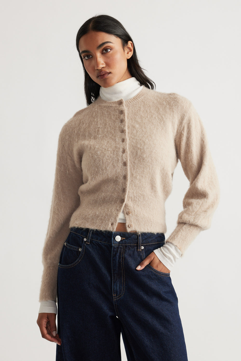 Woman wearing a soft beige Ariel Button Through Cardigan with balloon sleeves styled with dark high-waist denim jeans