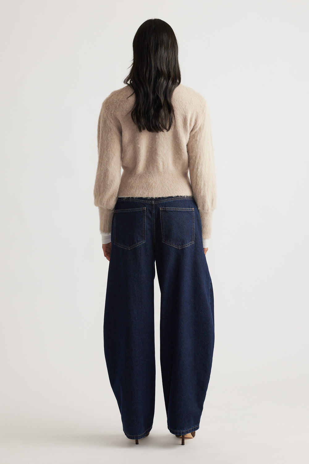 Back view of a woman wearing a soft beige Ariel Button Through Cardigan paired with wide-leg dark denim jeans by DECJUBA