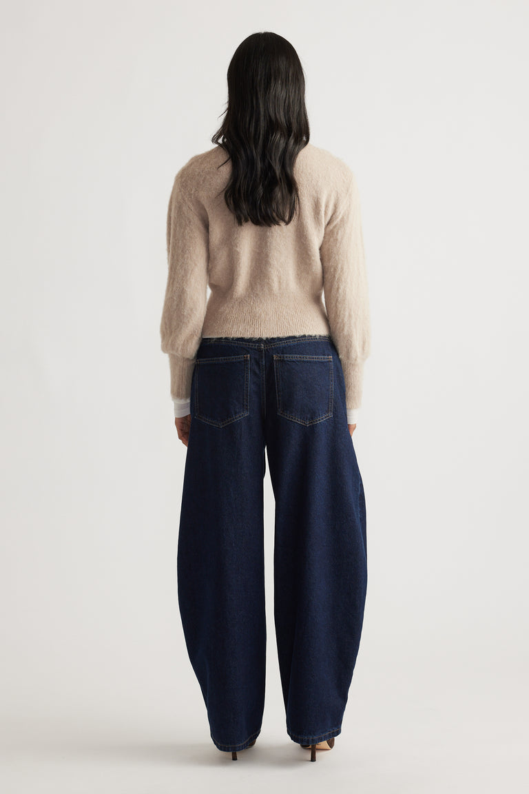 Back view of a woman wearing a soft beige Ariel Button Through Cardigan paired with wide-leg dark denim jeans by DECJUBA