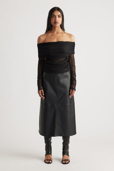 Woman wearing a black off-shoulder ruched mesh top paired with a high-waisted faux leather midi skirt and open-toe heels