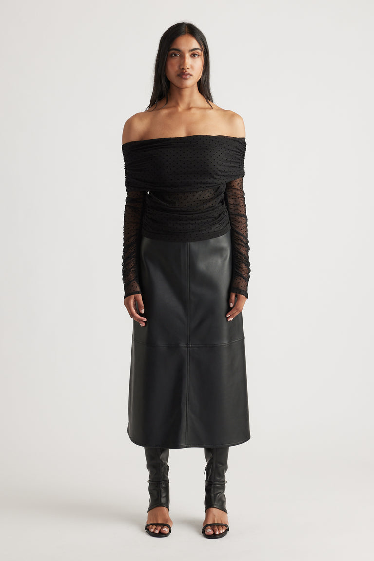 Woman wearing a black off-shoulder ruched mesh top paired with a high-waisted faux leather midi skirt and open-toe heels