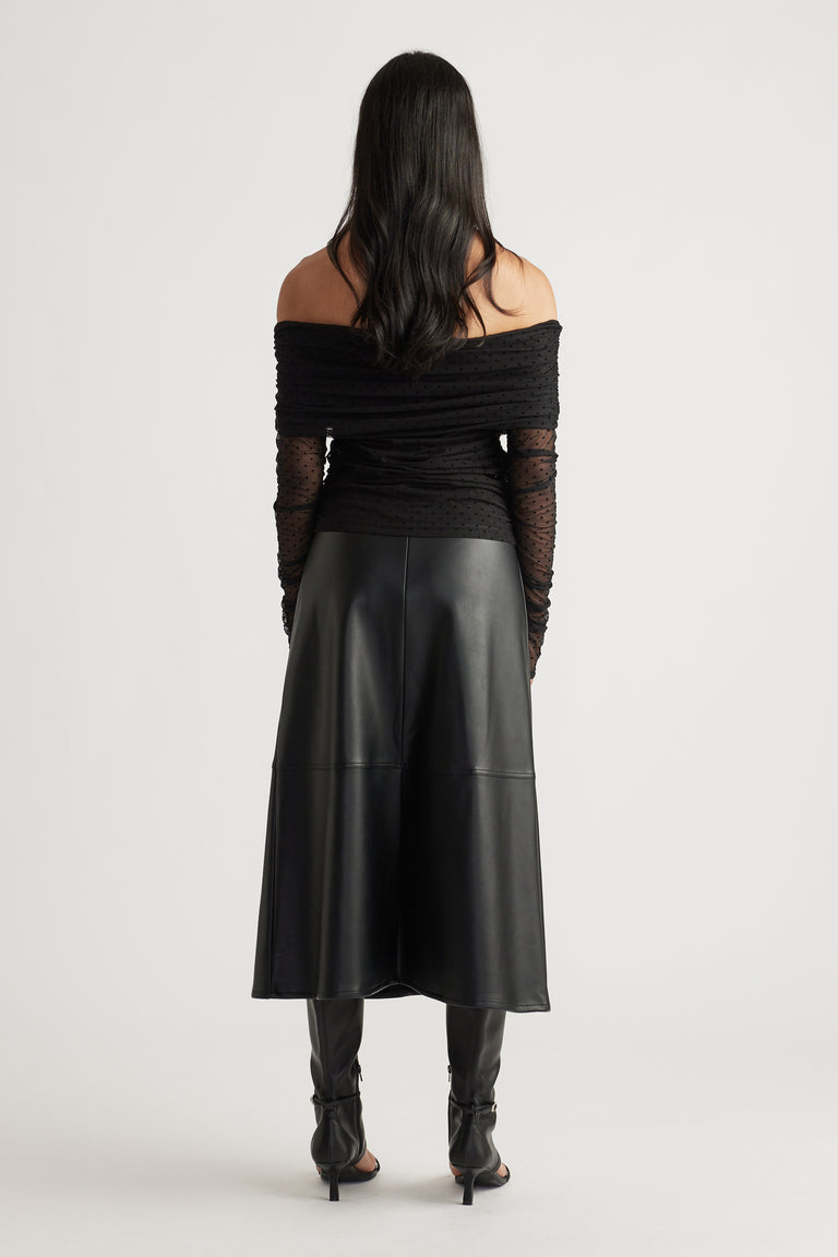 Back view of a woman wearing a fitted off-shoulder ruched mesh top with sheer sleeves, paired with a black midi skirt and heels