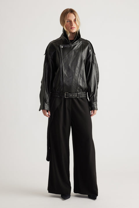 Woman wearing a black belted leather jacket styled with wide-leg black palazzo pants for a bold, modern look