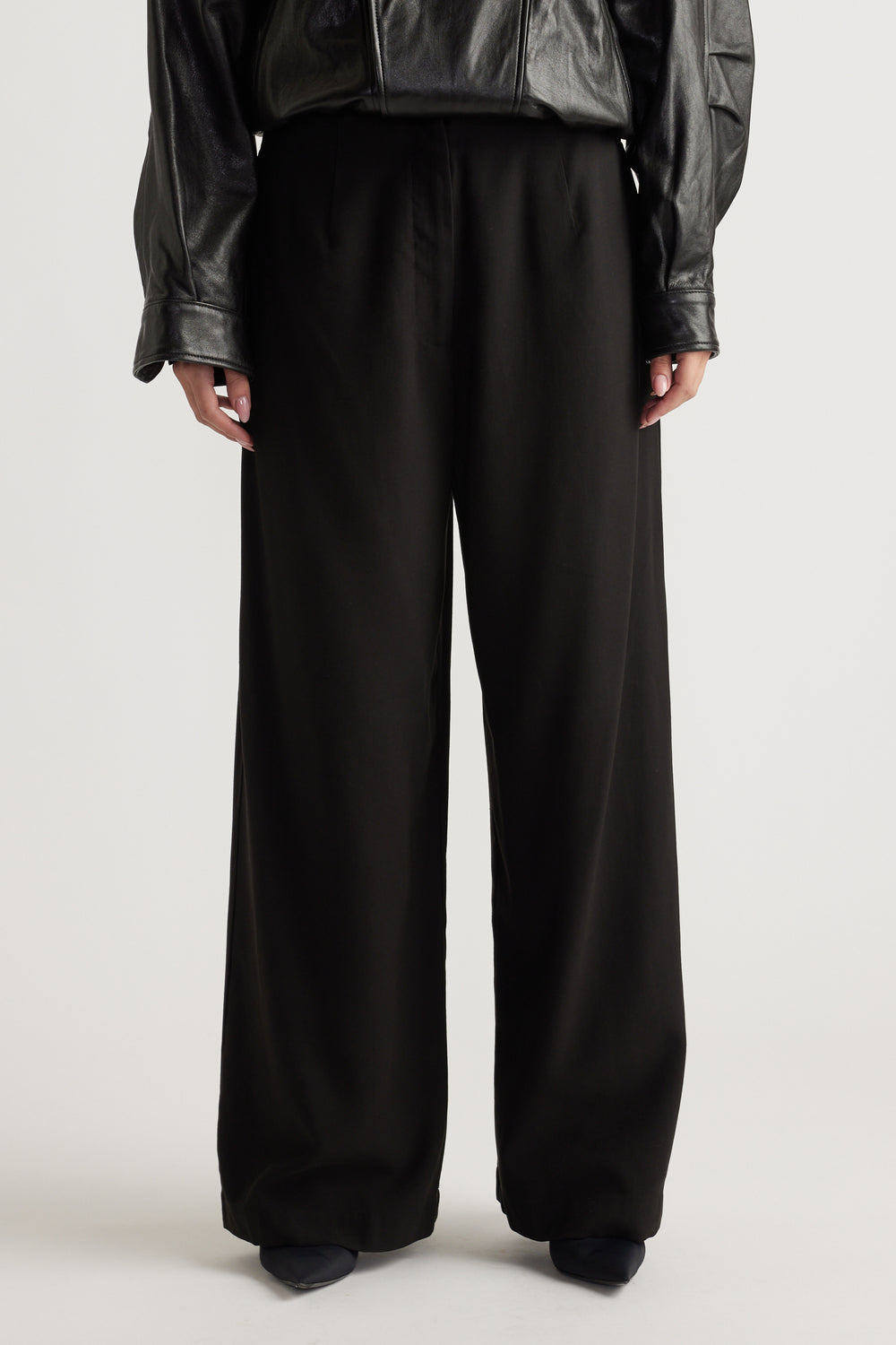 Front view of relaxed black wide-leg pants paired with a black faux leather top for a chic, effortless look.