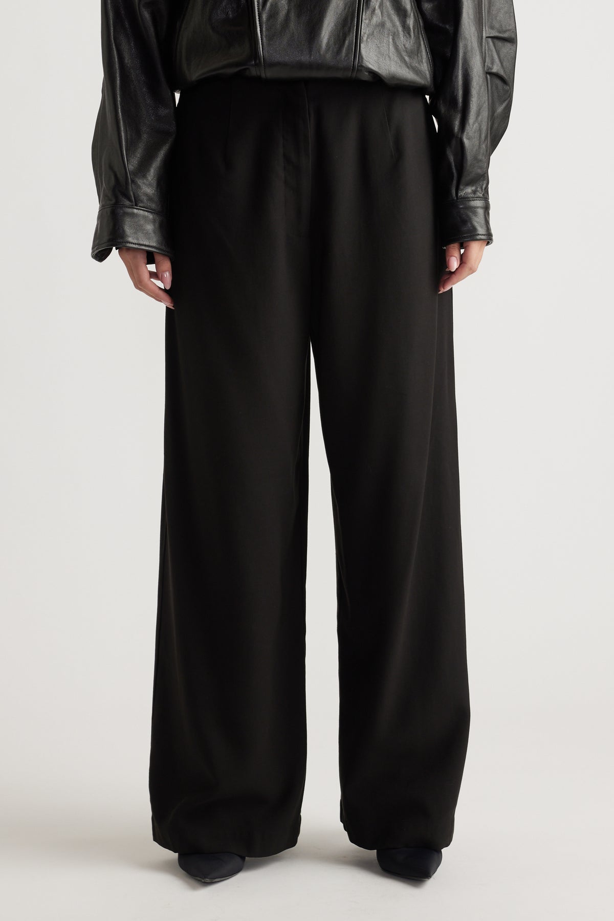 Front view of relaxed black wide-leg pants paired with a black faux leather top for a chic, effortless look.