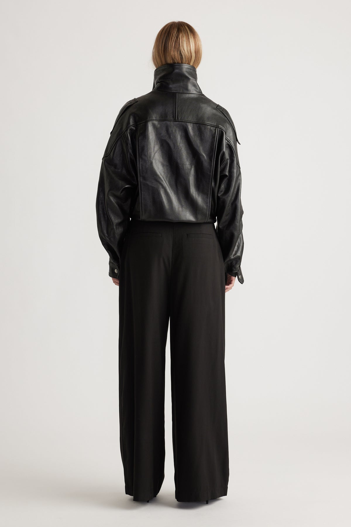 Woman wearing high-waisted black wide-leg palazzo pants paired with a cropped black leather jacket from the back view.