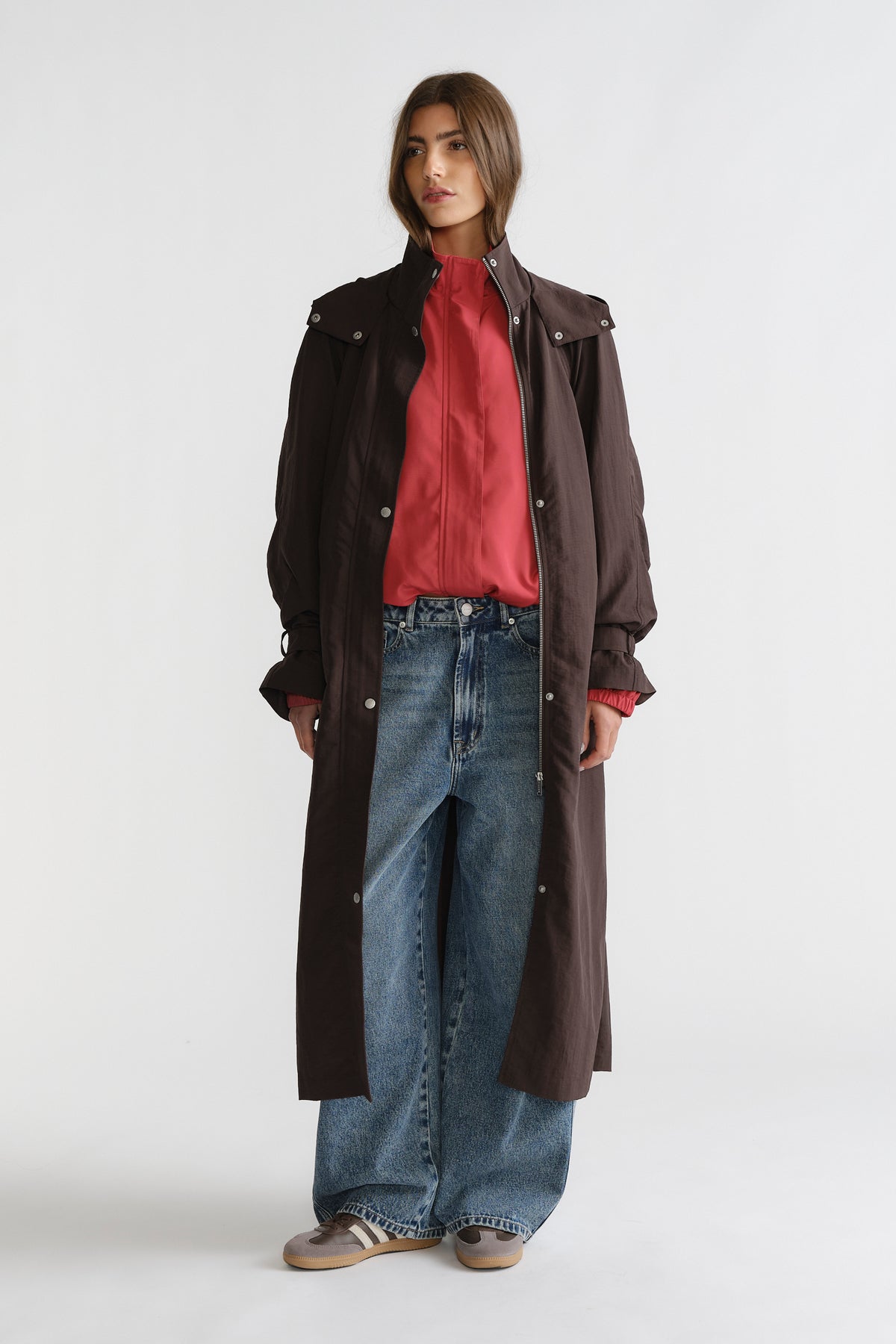 Woman wearing a cocoa brown D-Luxe Anorak layered over a rust-colored blouse with wide-leg blue jeans and casual sneakers