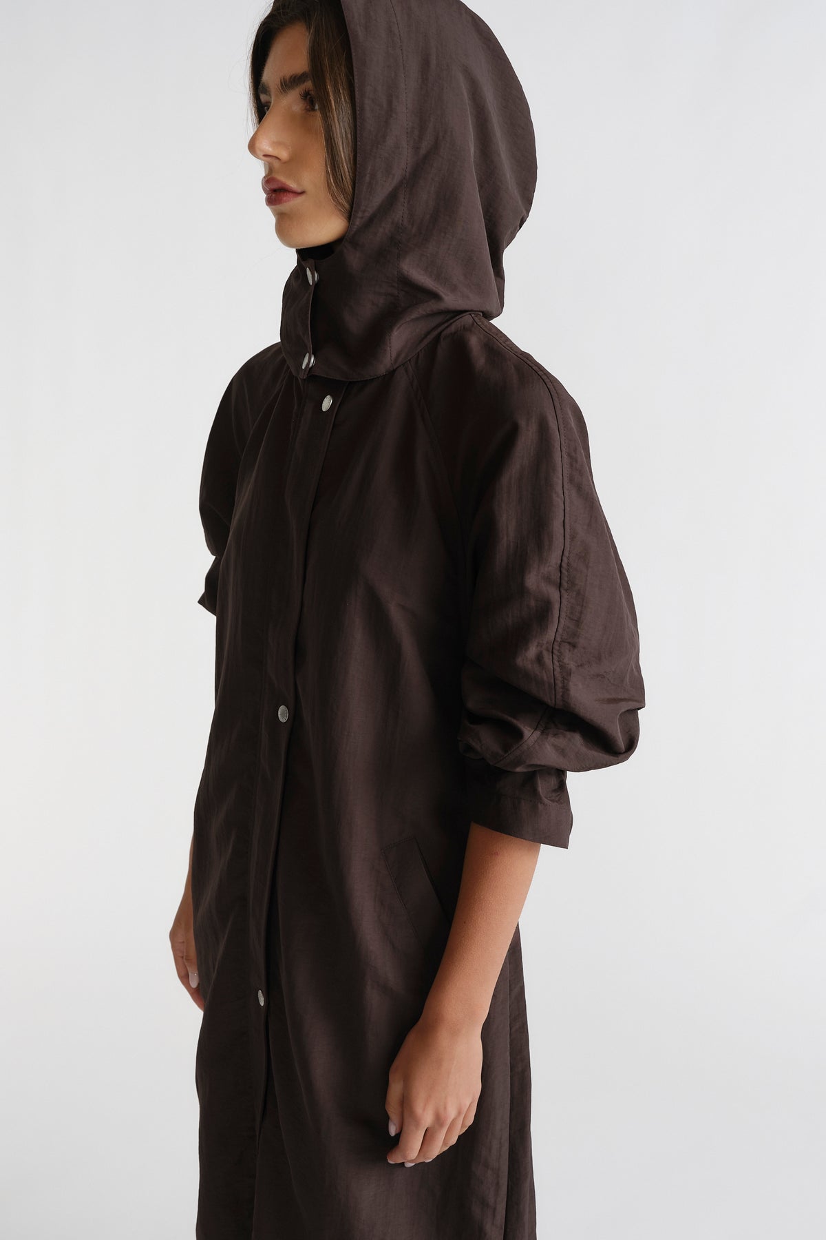 Woman in profile wearing a cocoa brown D-Luxe Anorak with a hood and relaxed sleeves, showcasing effortless style.