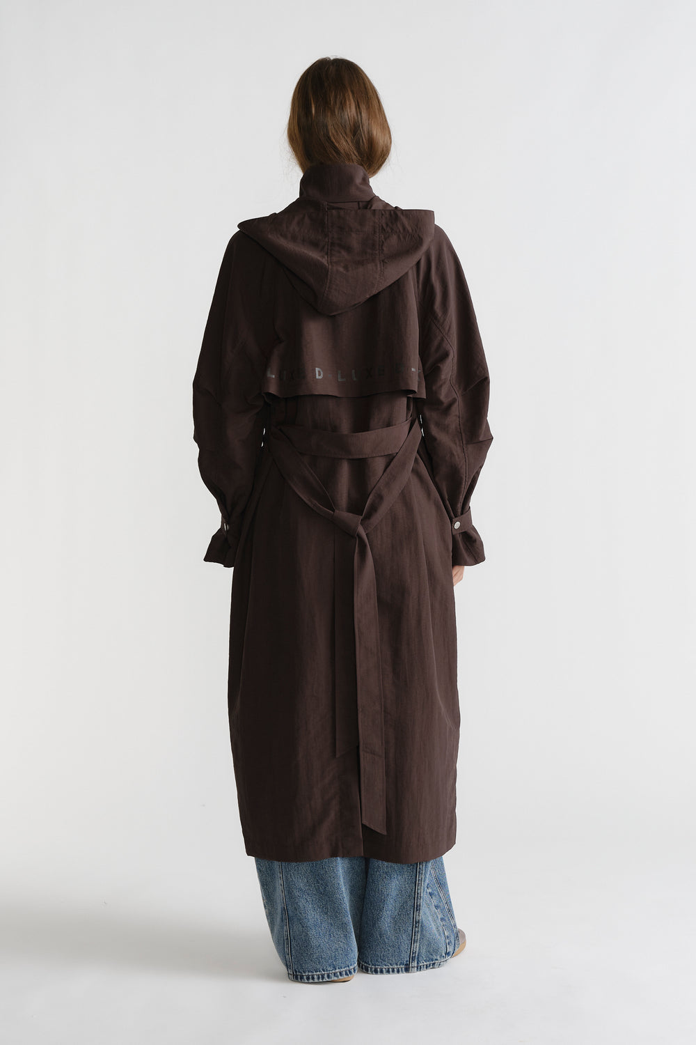 Woman seen from behind wearing cocoa brown D-Luxe Anorak with a belted waist paired with relaxed blue denim jeans.
