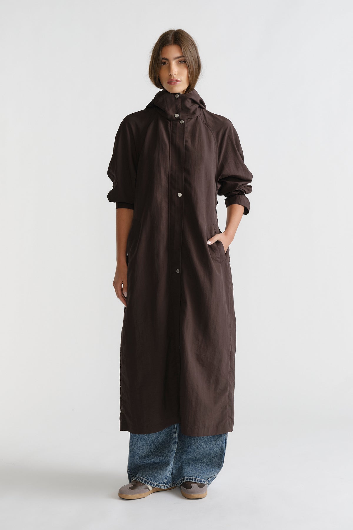 Woman wearing a cocoa brown D-Luxe Anorak with a hood and front snaps, styled with relaxed wide-leg denim jeans and casual shoes