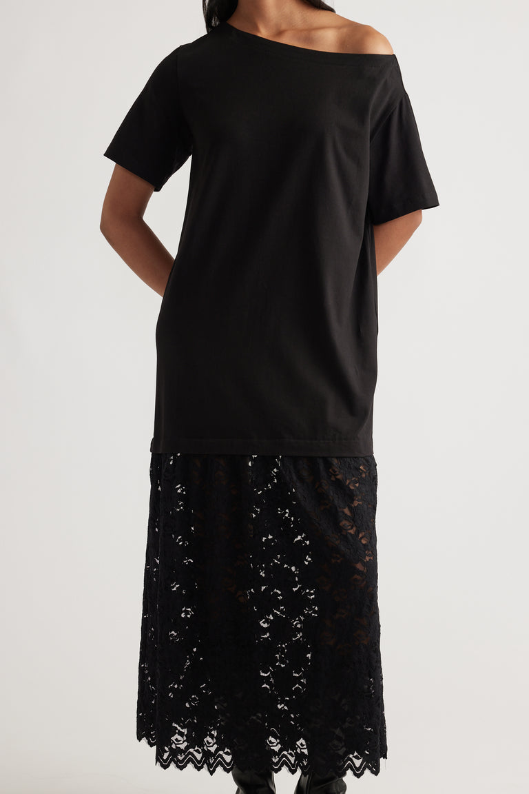Woman wearing an off-shoulder black top layered over a sheer lace midi skirt with floral detailing and scalloped hem