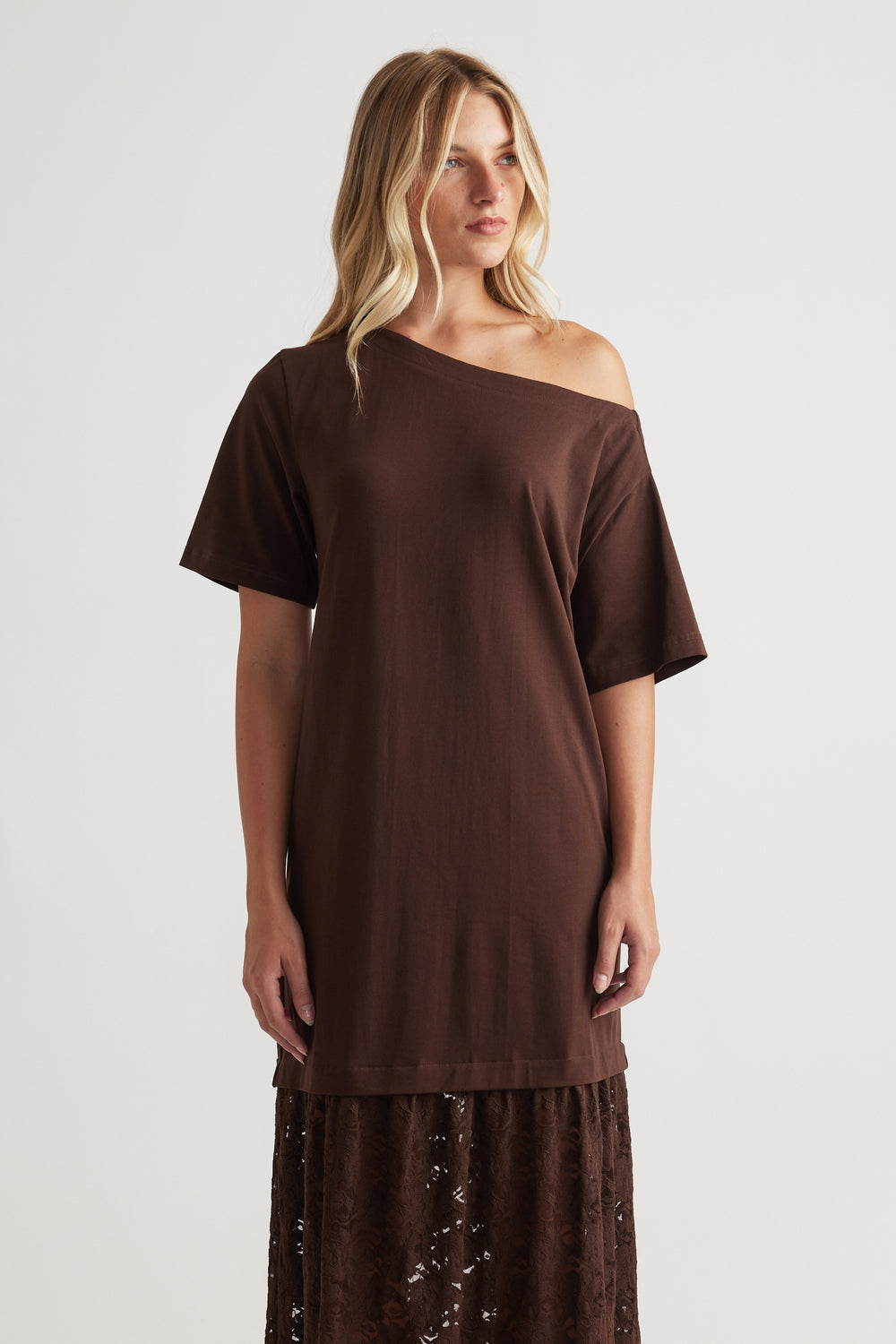 Woman wearing Alexis Lace Maxi Dress in rich mocha with a relaxed off-shoulder top and intricate lace skirt by DECJUBA.