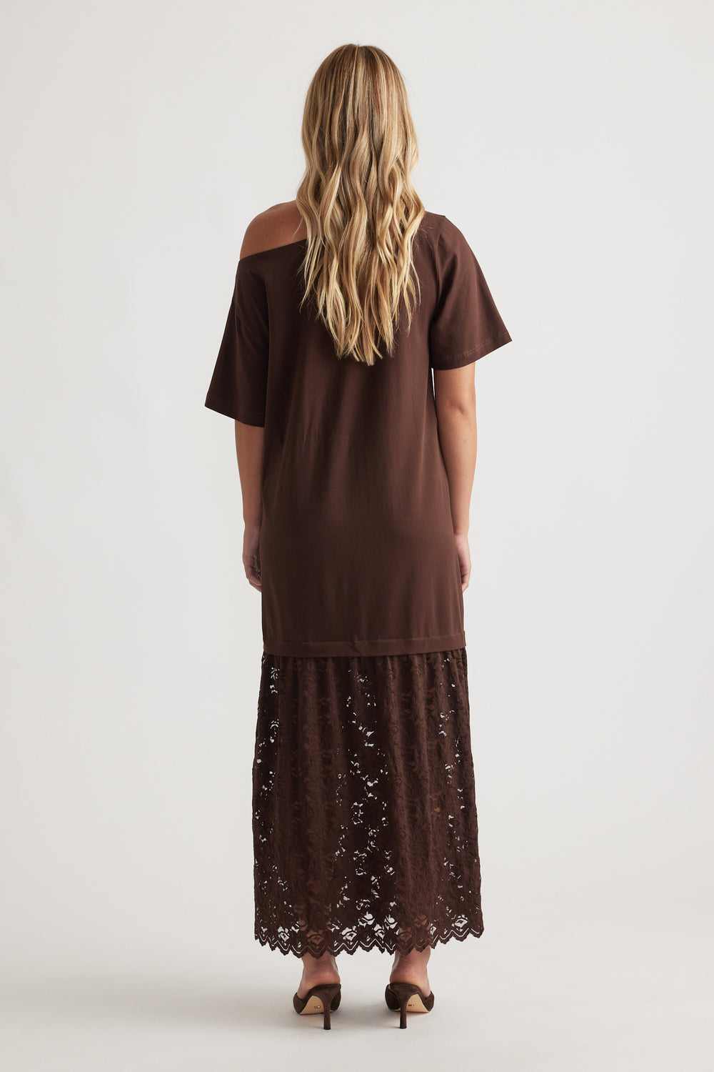 Woman wearing Alexis Lace Maxi Dress in rich mocha with relaxed fit top and intricate lace overlay skirt, paired with heels