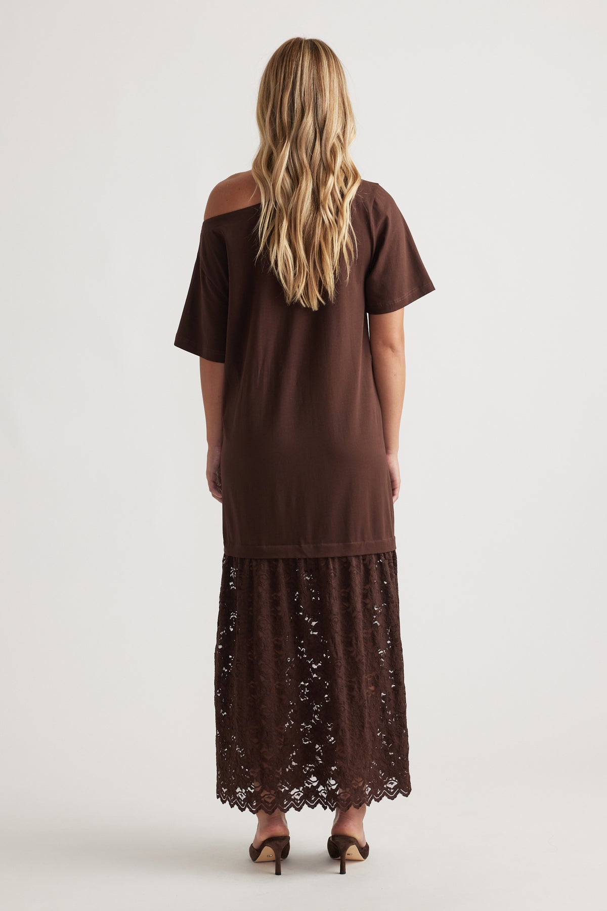 Woman wearing Alexis Lace Maxi Dress in rich mocha with relaxed fit top and intricate lace overlay skirt, paired with heels
