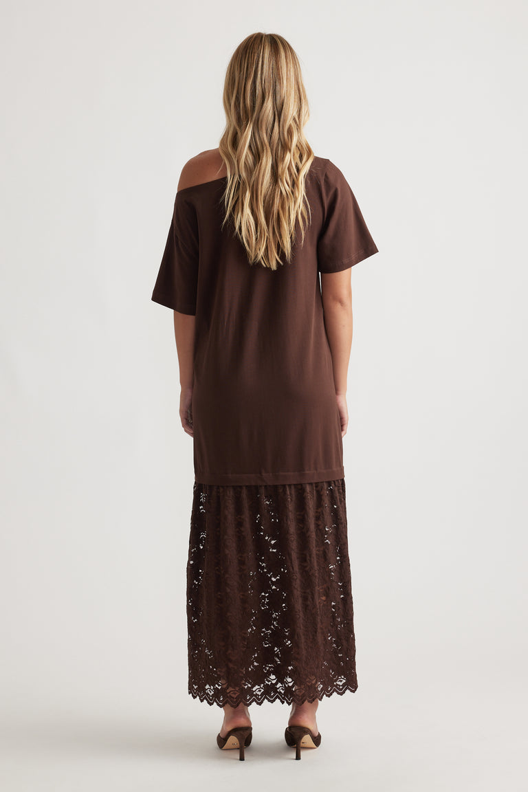 Woman wearing Alexis Lace Maxi Dress in rich mocha with relaxed fit top and intricate lace overlay skirt, paired with heels
