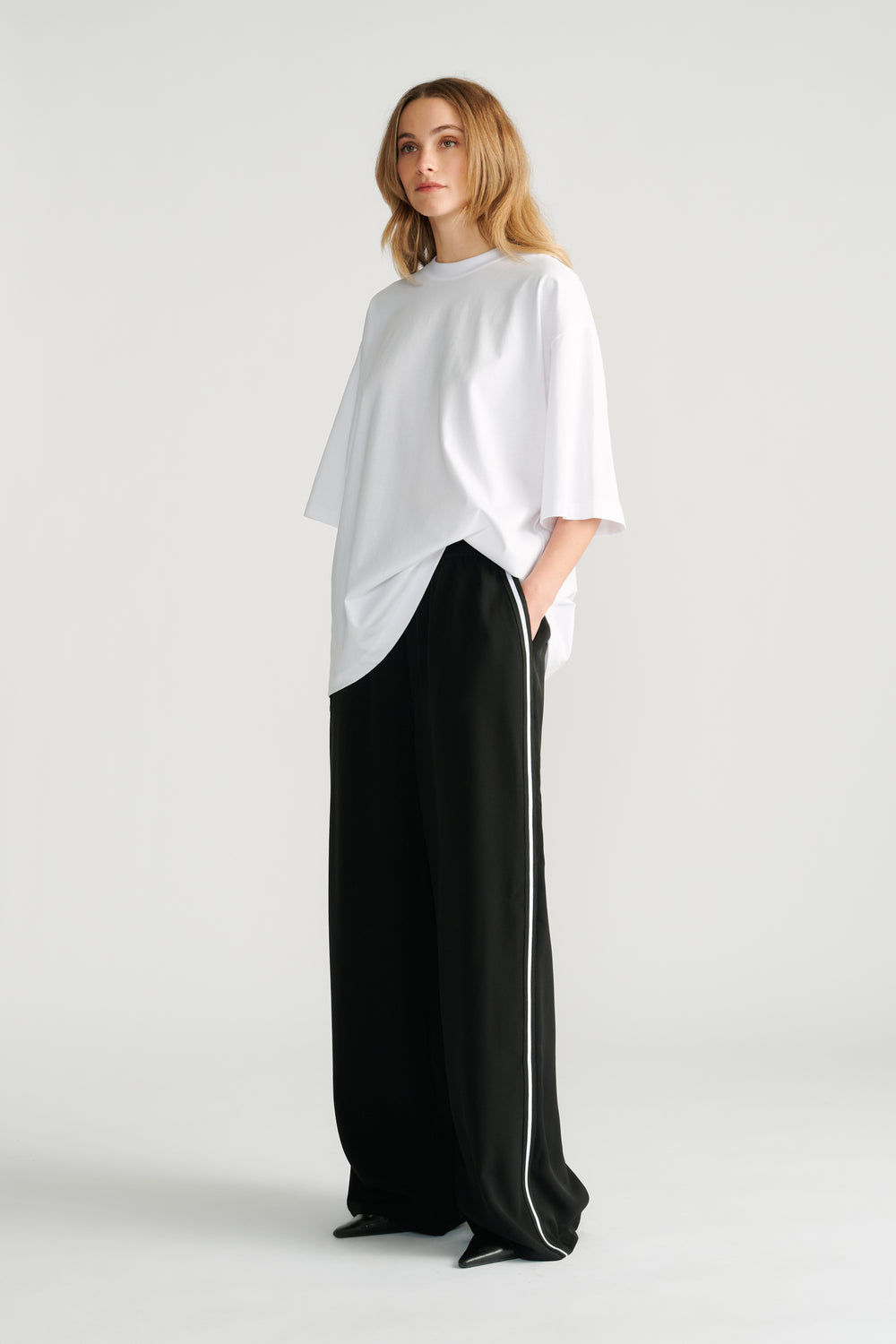 Woman wearing relaxed black wide-leg pants with white side stripe paired with an oversized white tee for a casual look.