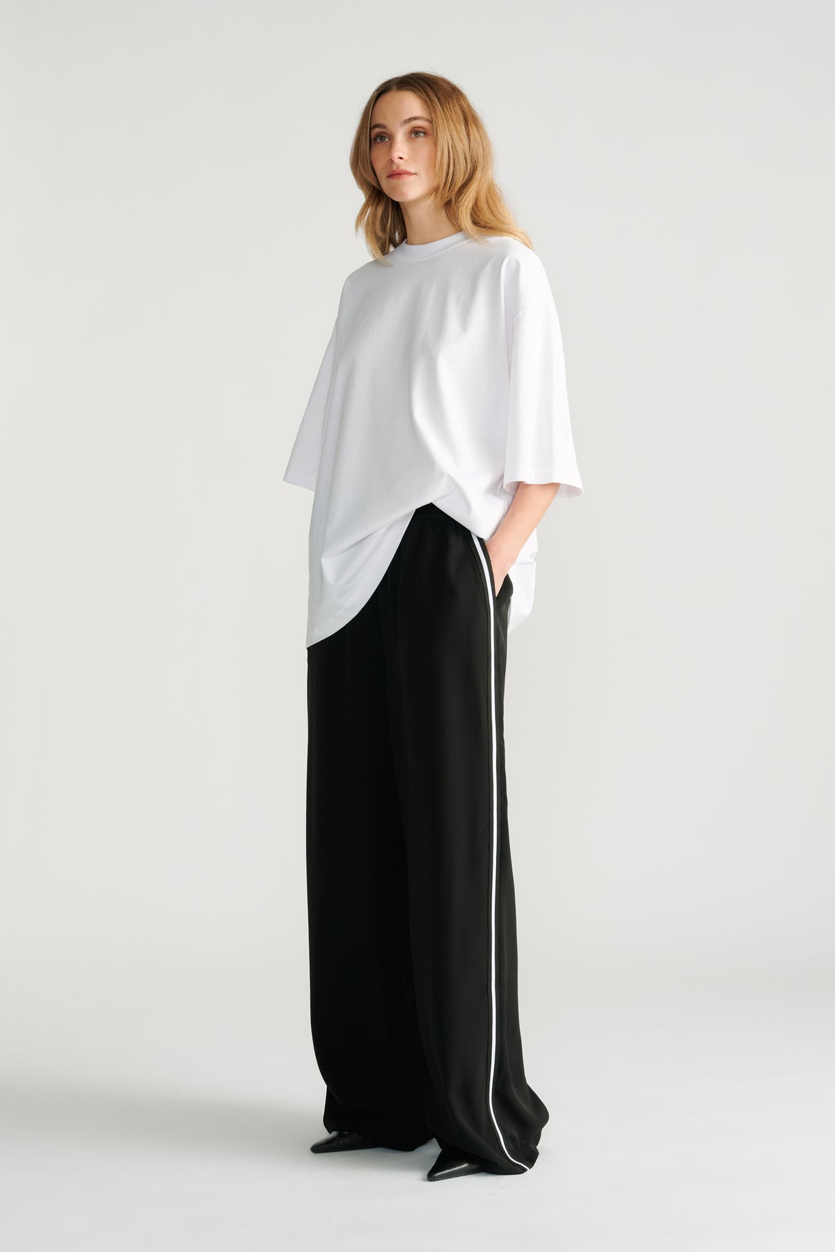 Woman wearing relaxed black wide-leg pants with white side stripe paired with an oversized white tee for a casual look.