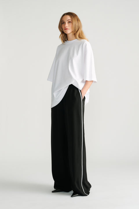 Woman wearing relaxed black wide-leg pants with white side stripe paired with an oversized white tee for a casual look.