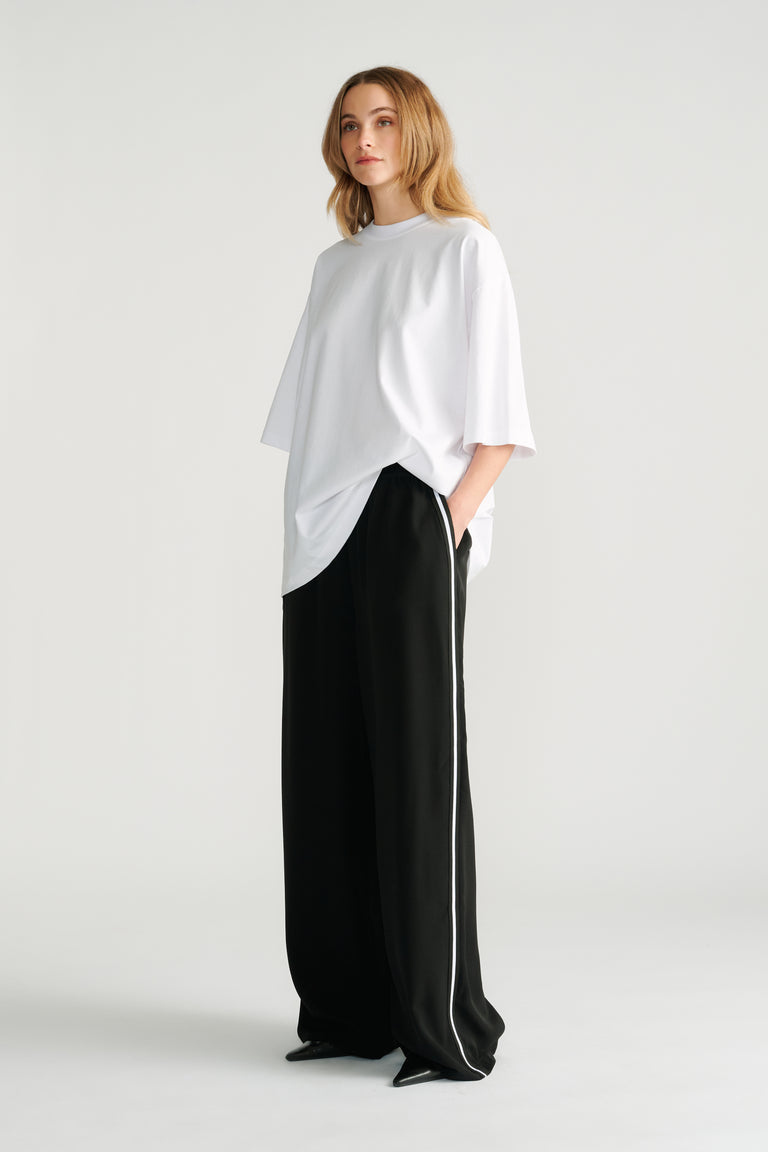 Woman wearing relaxed black wide-leg pants with white side stripe paired with an oversized white tee for a casual look.