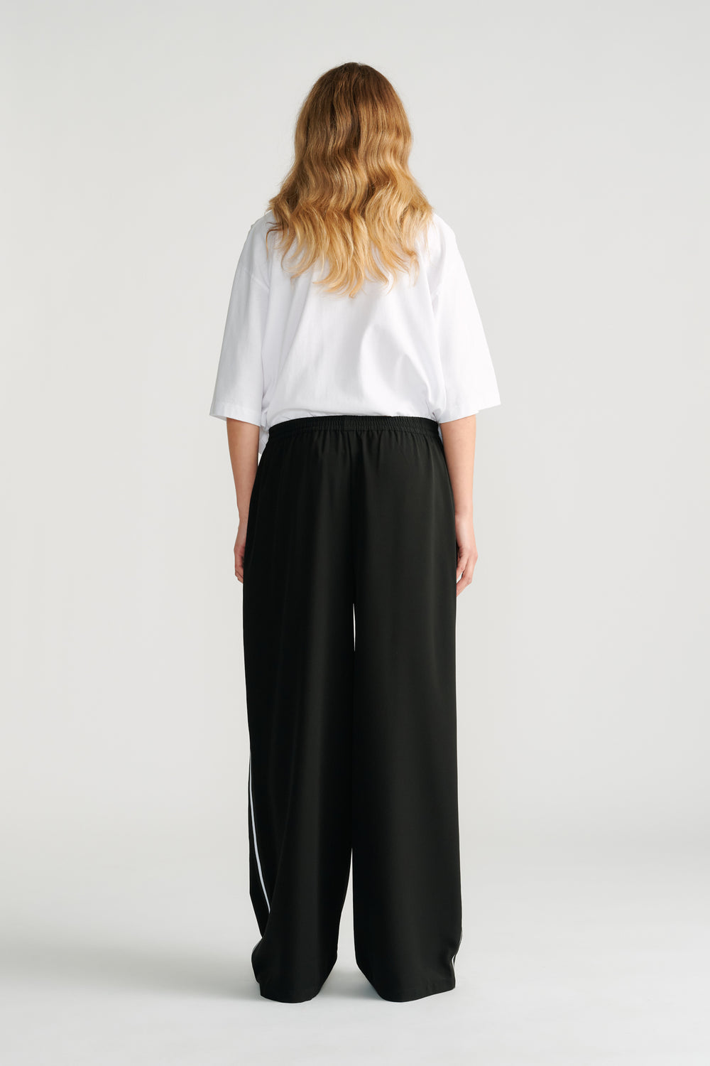 Woman wearing black wide-leg twill pants with a white side stripe paired with a loose white short-sleeve top.