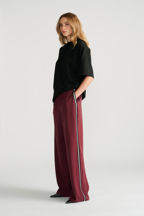 Woman wearing relaxed plum twill pants with a contrasting side stripe and a loose black short-sleeve top.