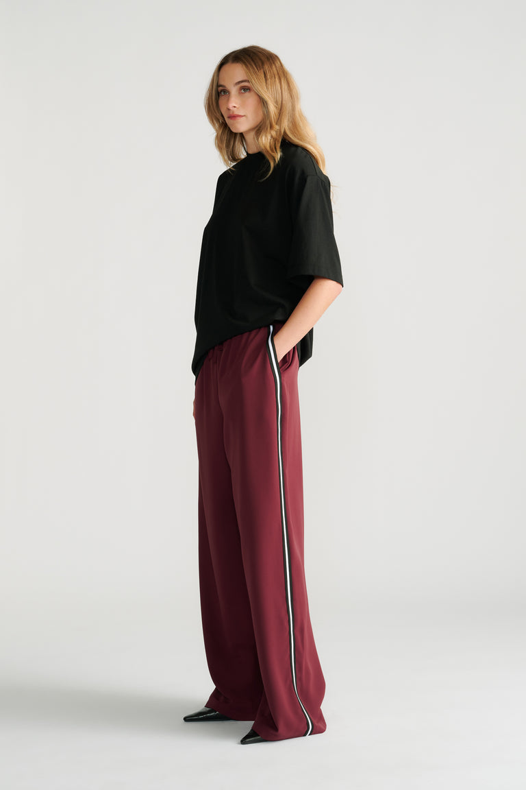 Woman wearing relaxed plum twill pants with a contrasting side stripe and a loose black short-sleeve top.