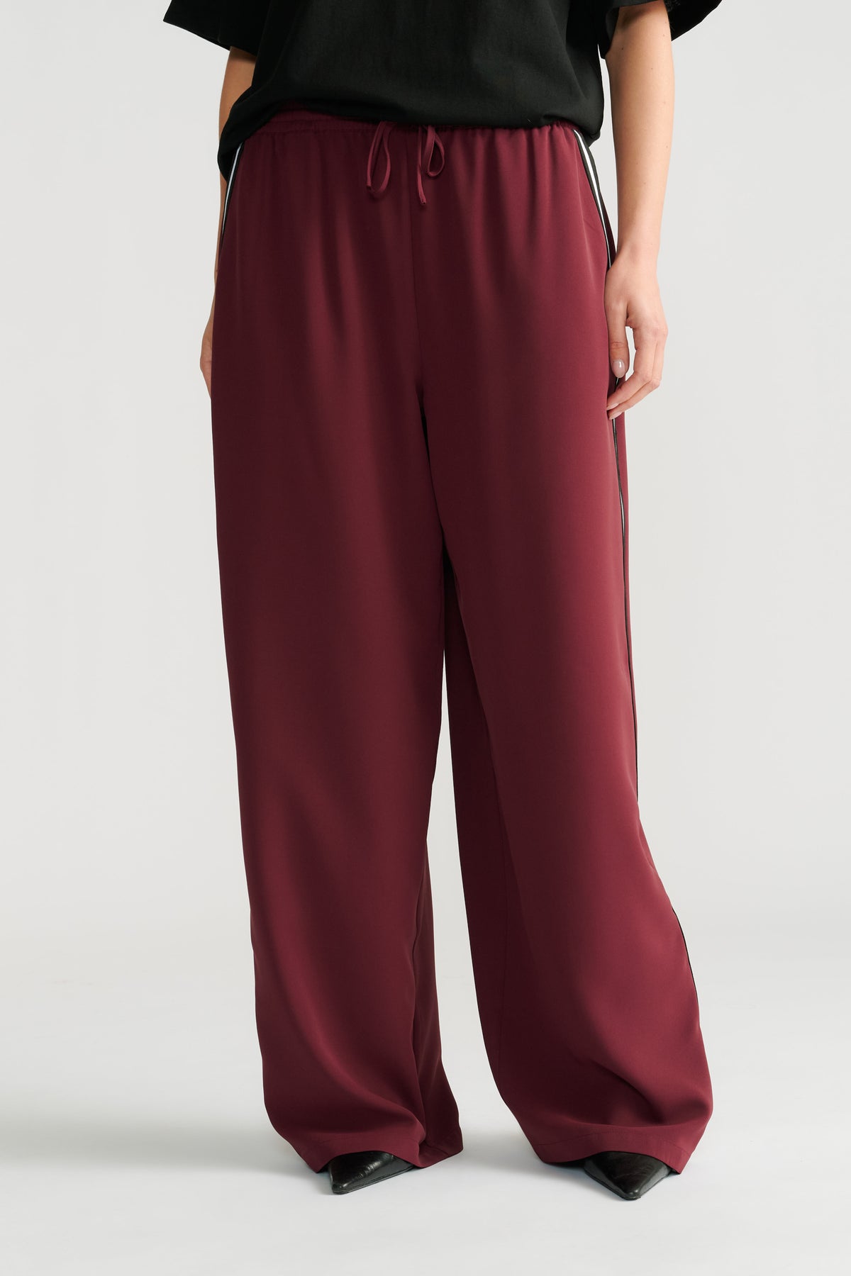 Wide-leg plum twill pants with a side stripe detail and a comfortable drawstring waist, styled with black pointed shoes.