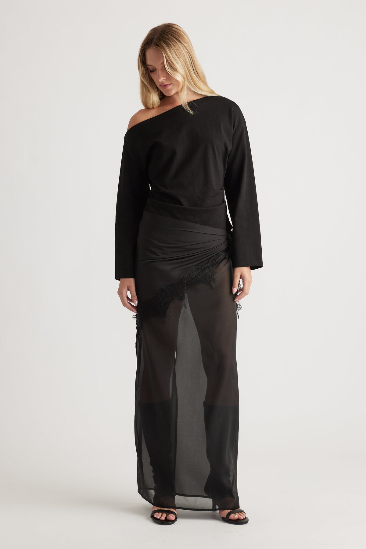 Woman wearing an off-shoulder black long sleeve top paired with a sheer black maxi skirt featuring lace trim details
