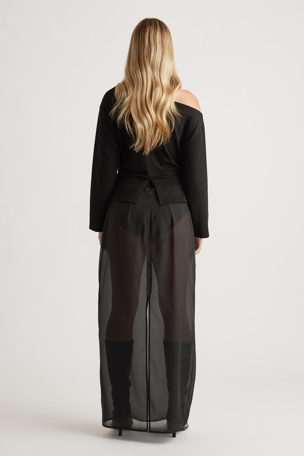 Woman wearing a black off-shoulder top paired with sheer wide-leg pants and knee-high black boots for a bold look