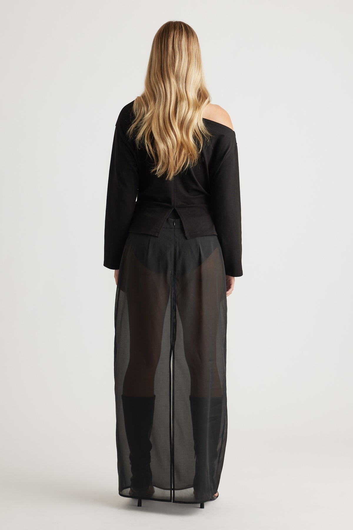 Woman wearing a black off-shoulder top paired with sheer wide-leg pants and knee-high black boots for a bold look