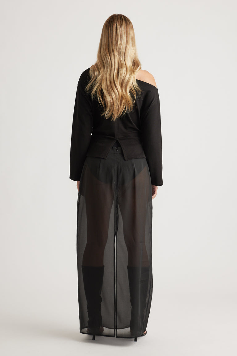 Woman wearing a black off-shoulder top paired with sheer wide-leg pants and knee-high black boots for a bold look