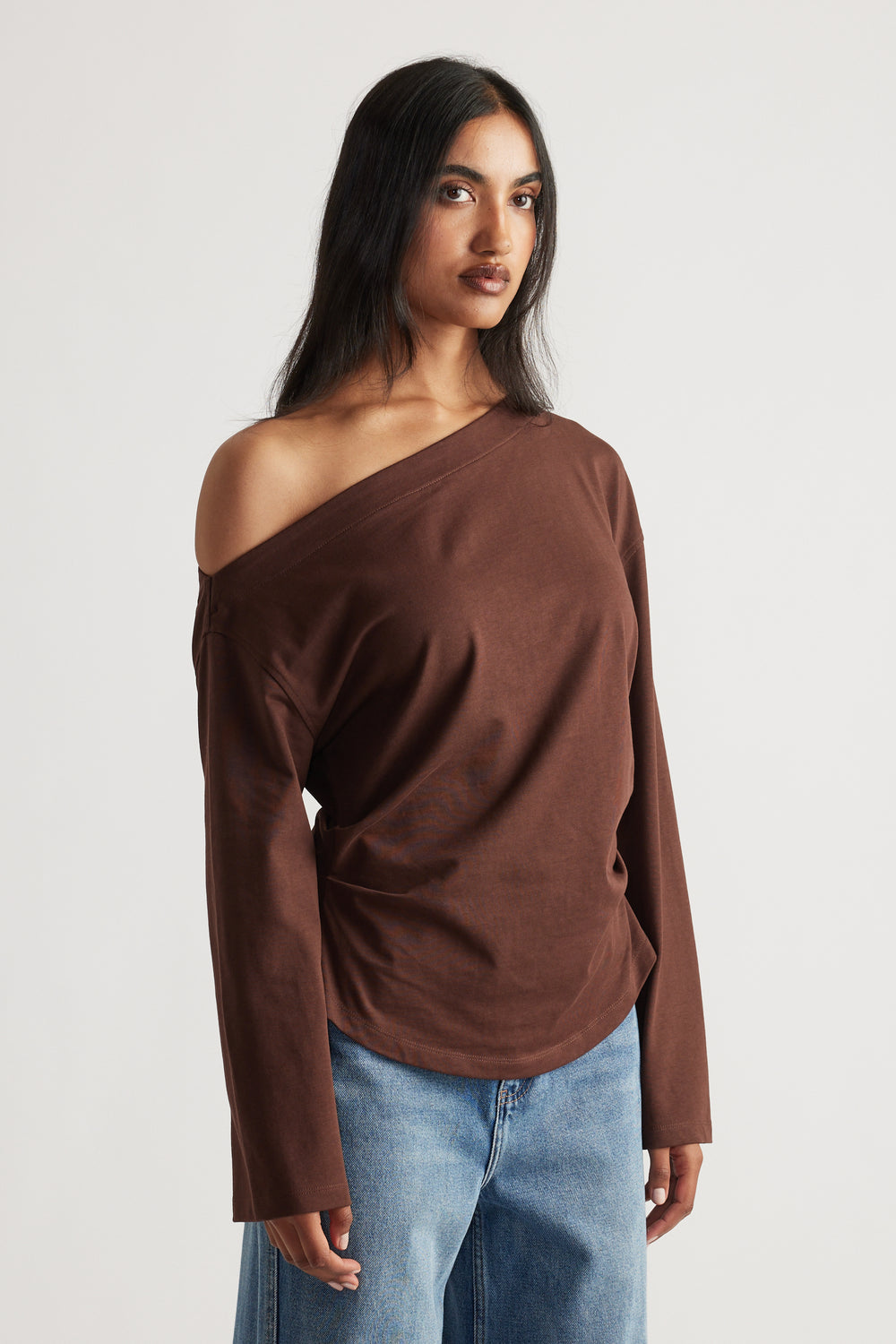 Woman wearing a relaxed-fit brown off-shoulder long sleeve tee paired with light blue wide-leg denim jeans.