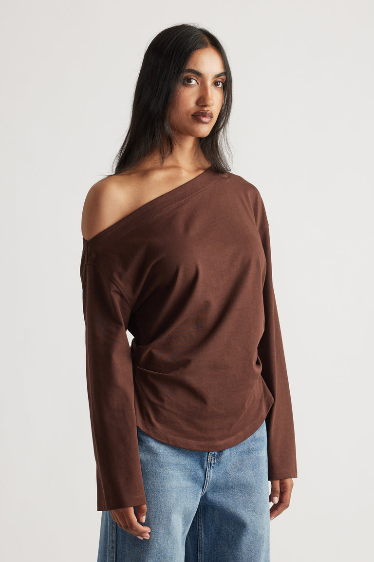 Woman wearing a relaxed-fit brown off-shoulder long sleeve tee paired with light blue wide-leg denim jeans.