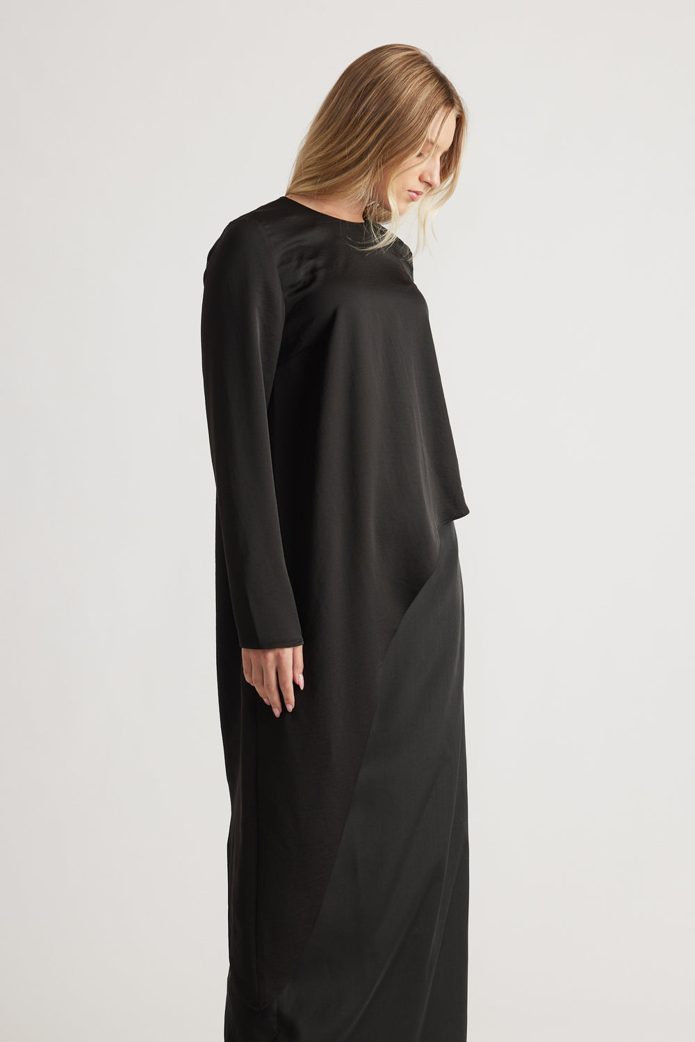 Woman wearing a sleek black satin drape top with long sleeves, paired with a matching black skirt for a minimalist look