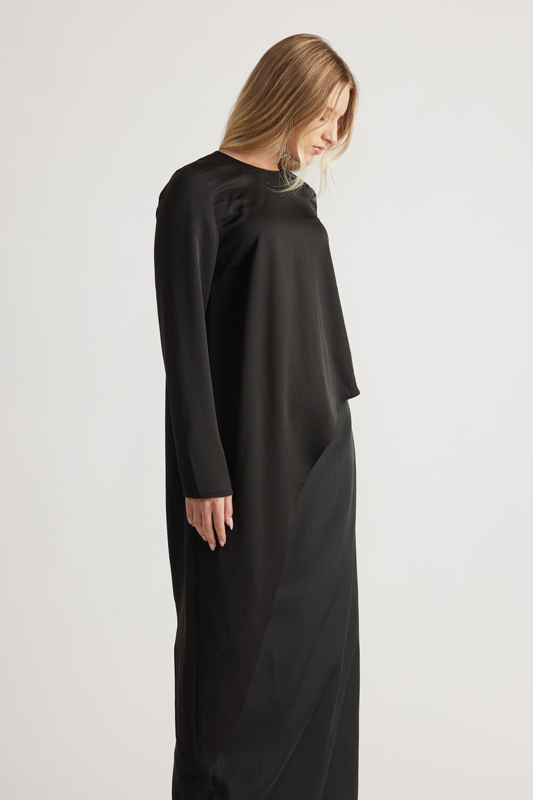 Woman wearing a sleek black satin drape top with long sleeves, paired with a matching black skirt for a minimalist look