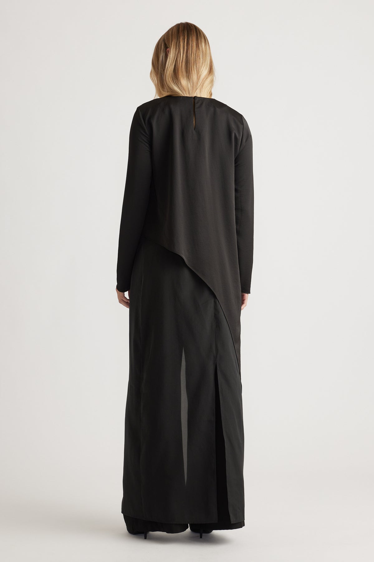 Back view of a woman wearing a black satin drape top paired with wide-leg black pants for a sleek look