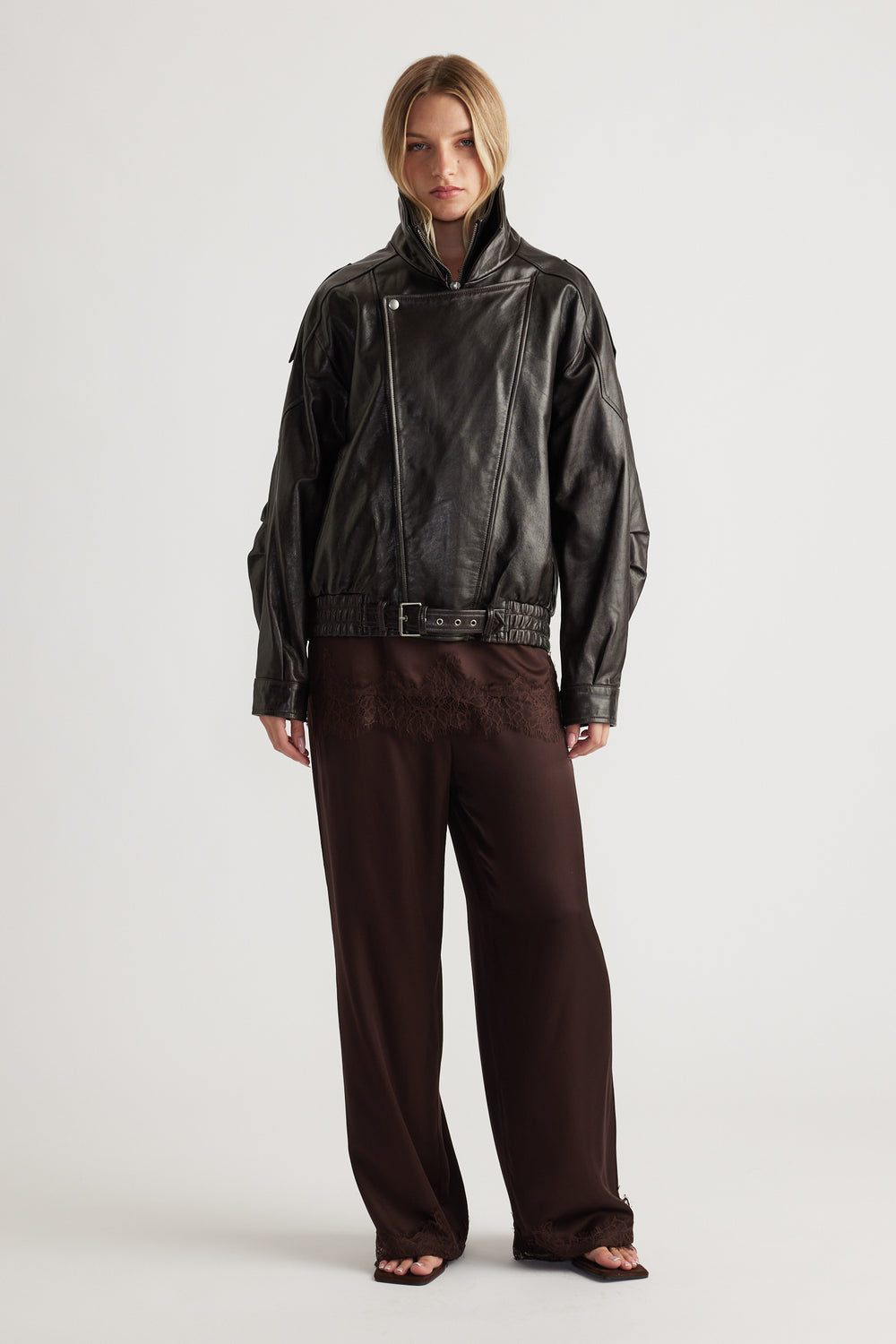 Woman wearing a dark brown satin pant with lace trim paired with a black leather jacket for an edgy, elegant look