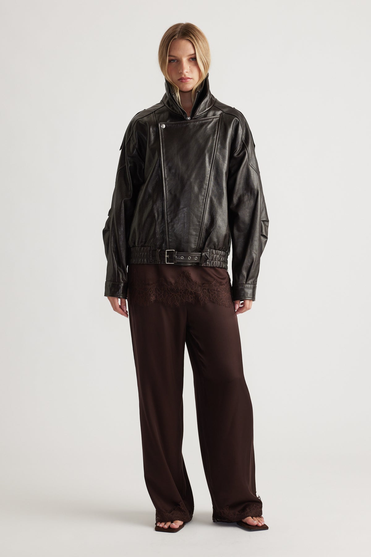 Woman wearing a dark brown satin pant with lace trim paired with a black leather jacket for an edgy, elegant look