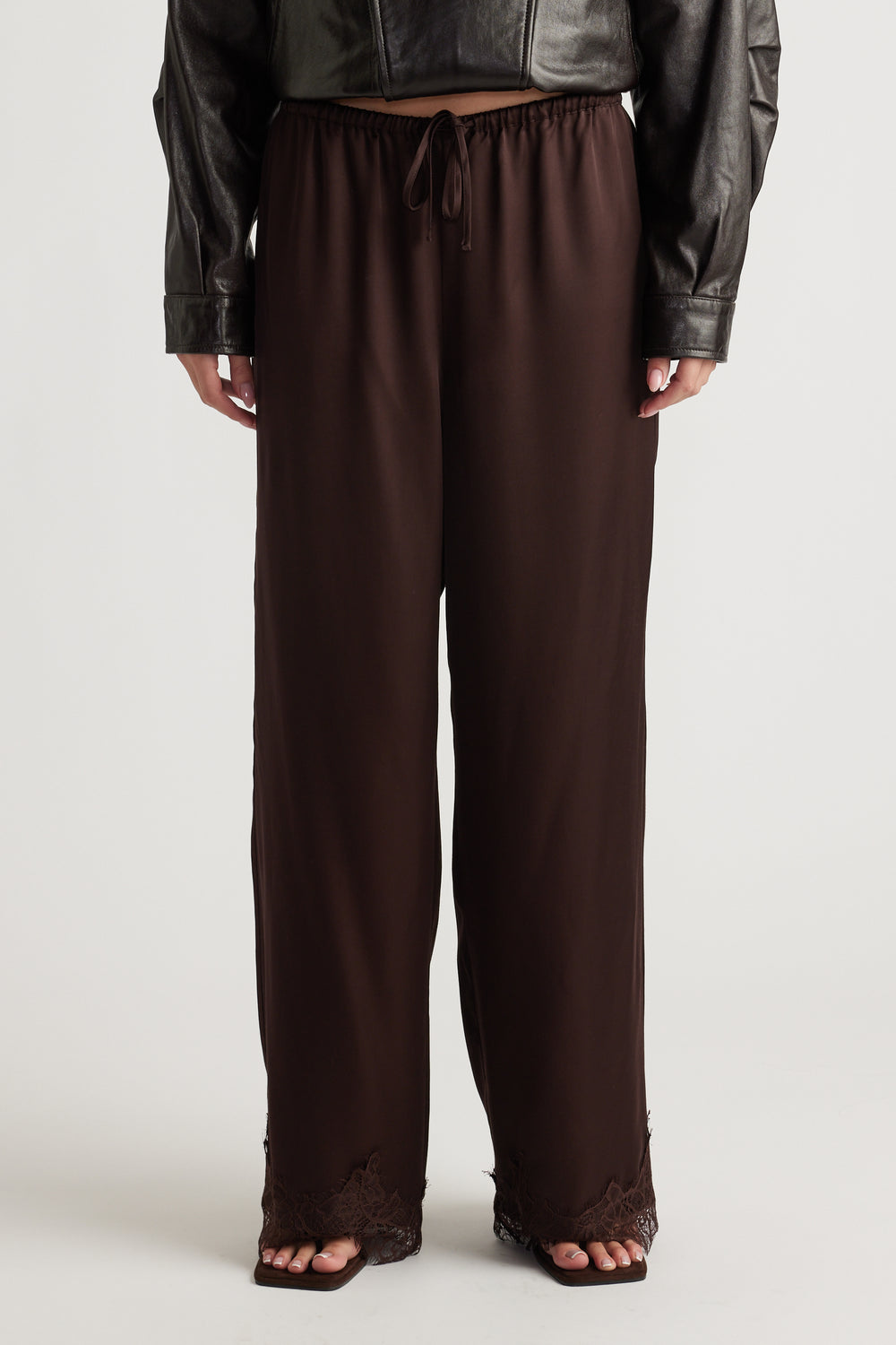 Dark brown satin pants with relaxed fit and delicate lace trim at the wide hems for a chic, comfortable look.