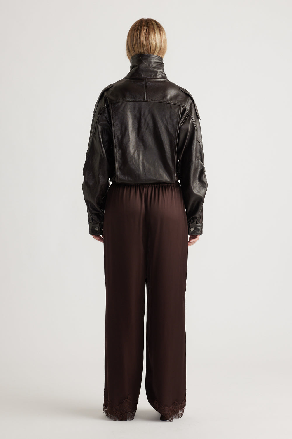 Back view of rich brown satin pants with lace trim at the hem, styled with a cropped black leather jacket