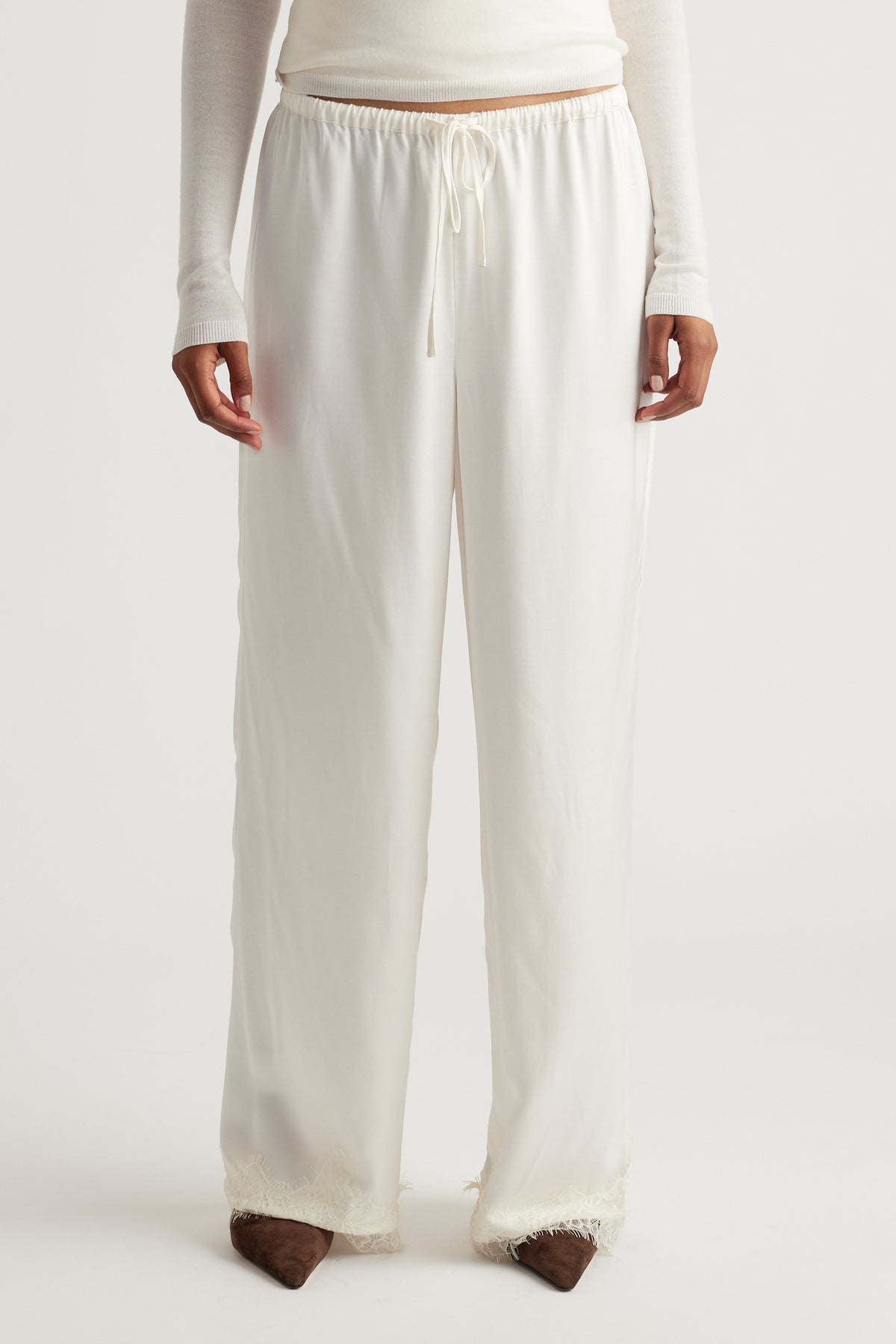 Front view of a woman wearing loose, ivory satin pants with delicate lace trim at the hem, styled with a fitted long-sleeve top